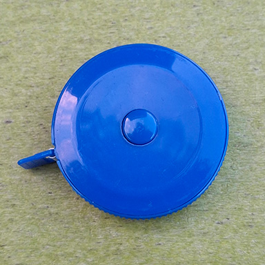 Its made out of a glossy blue plastic and while overall the shape is pretty primary there are details like the striped band around it, the button on top, and the tab to pull the tape